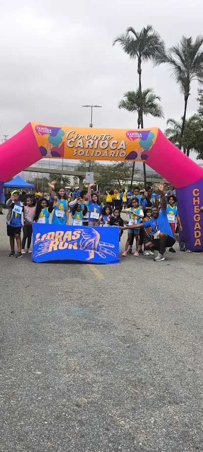 Arco rosa de chegada do Libras Run Kids, com crianças e famílias reunidas ao fundo