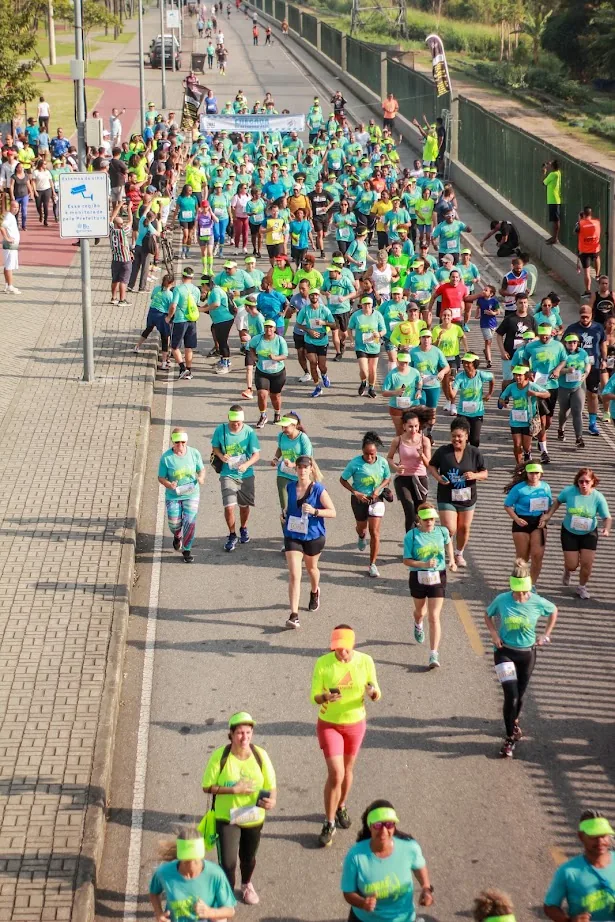 Pelotão de corredores de camisetas verdes e azuis na pista do Parque Madureira, visto de cima