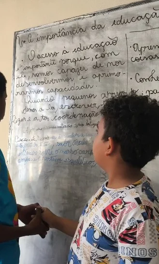 Criança escrevendo no quadro durante uma atividade de produção de texto no reforço