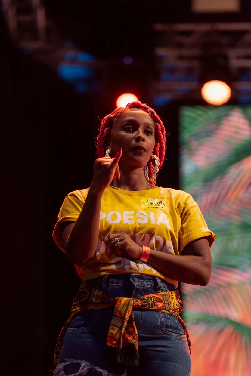 Suanne Gonçalves interpretando em Libras no palco, de camiseta amarela